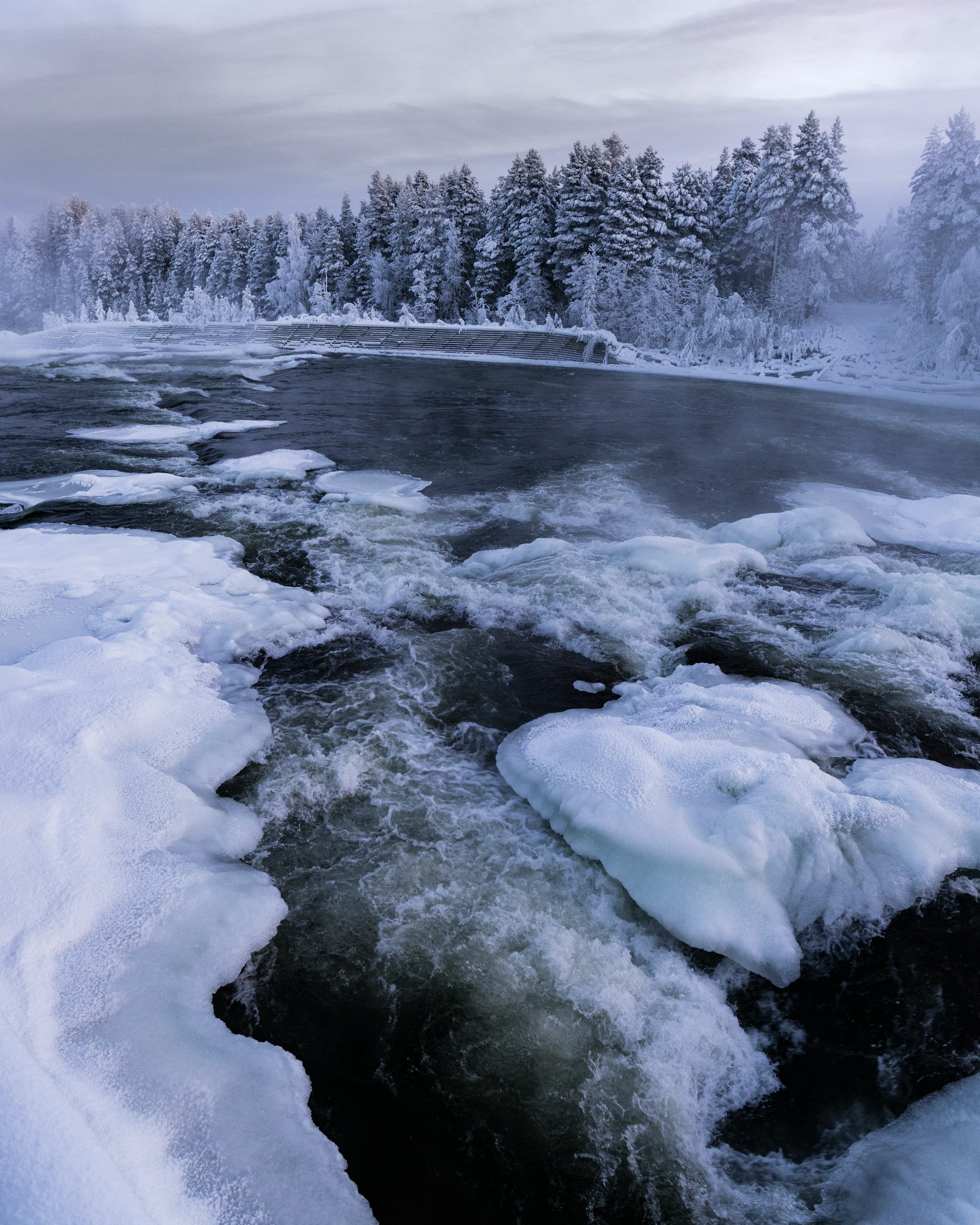 Icy winter river with rushing water between snow-covered banks and frosted trees