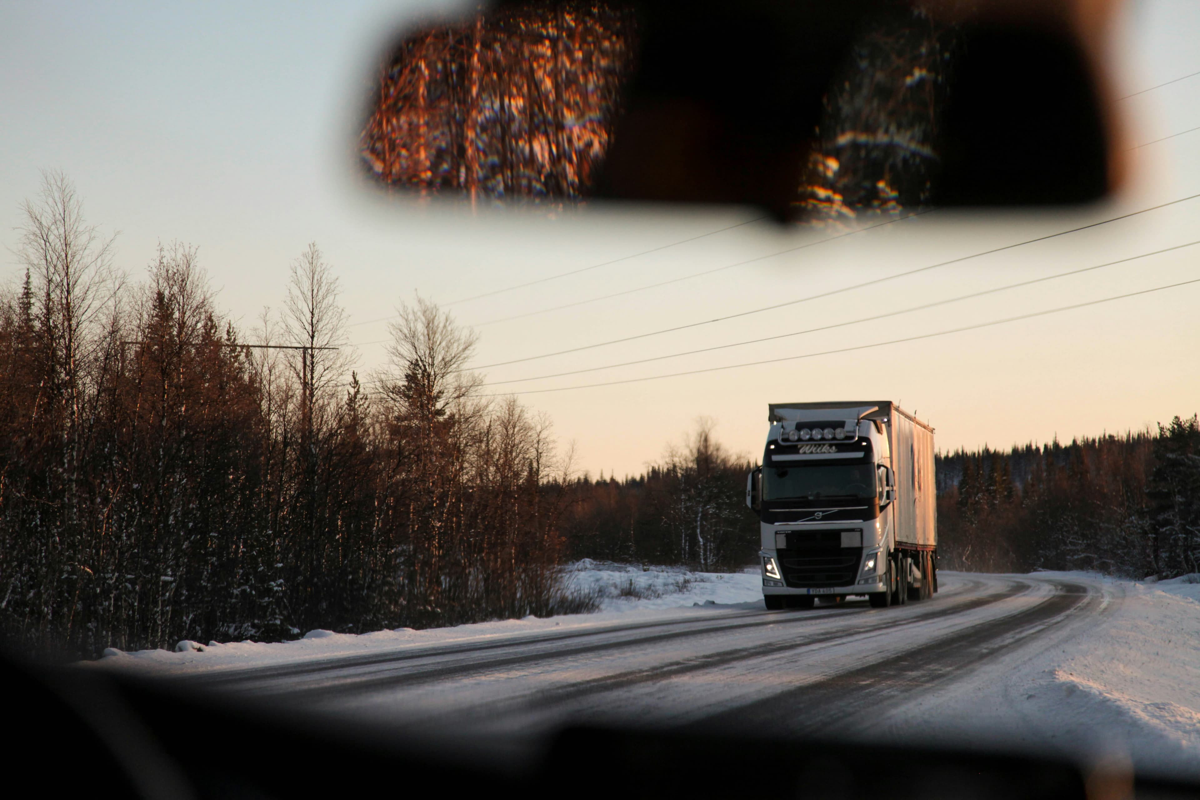 A semi truck driving on an icy winter road at sunset, seen from inside a car